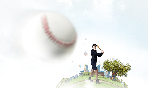 Young woman in suit and cylinder hitting ball with baseball bat