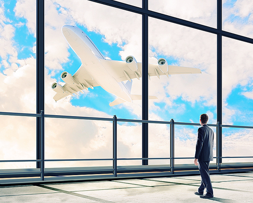 Image of businessman at airport looking at airplane taking off
