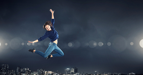 Young woman dancer jumping in spotlights on dark background