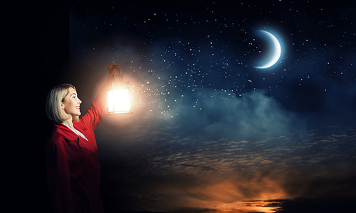 Young blonde in red cloak with lantern in darkness