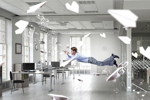 Young businessman flying in office and playing fife
