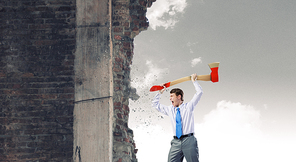 Young determined businessman crashing wall with axe