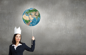 Young businesswoman in paper crown holding Earth planet balloon. Elements of this image are furnished by NASA