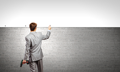 Rear view of businessman fixing blank white banner on wall