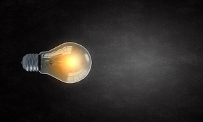 Glowing light bulb on dark background hanging from above