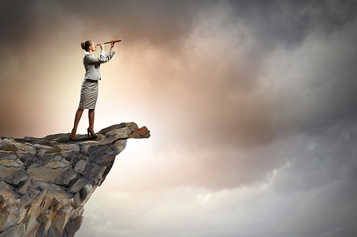 Image of businesswoman looking in telescope standing atop of rock