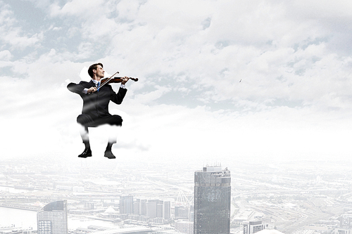 Young businessman sitting on cloud and playing violin