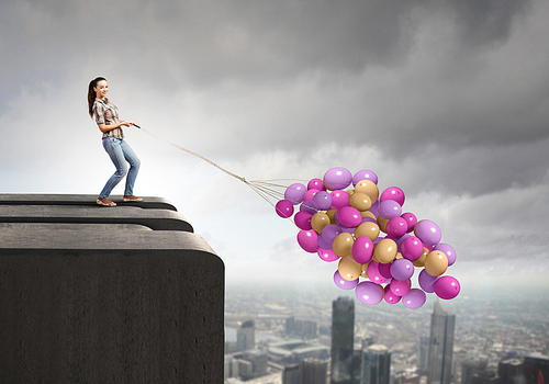 Young woman in casual holding bunch of colorful balloons