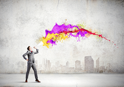 Young businessman speaking in trumpet and colorful splashes flying out