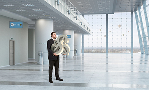 Young businessman in office interior carrying dollar sign