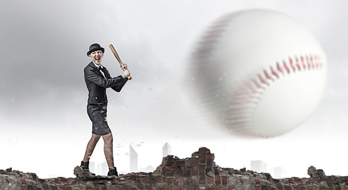 Young woman in suit and cylinder hitting ball with baseball bat