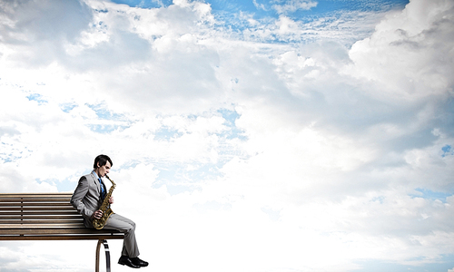 Young man sitting on wooden bench and playing saxophone
