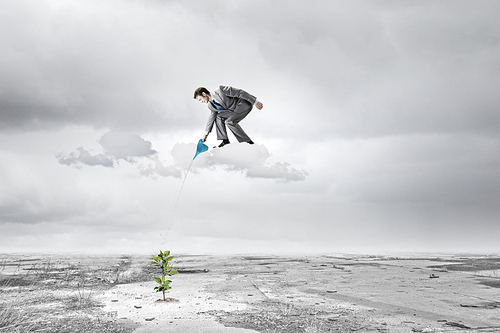 Young businessman standing on cloud and watering sprout