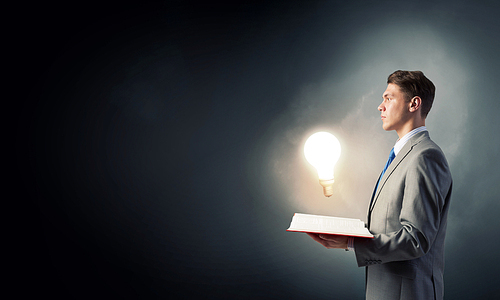 Businessman holding opened book with glass glowing light bulb