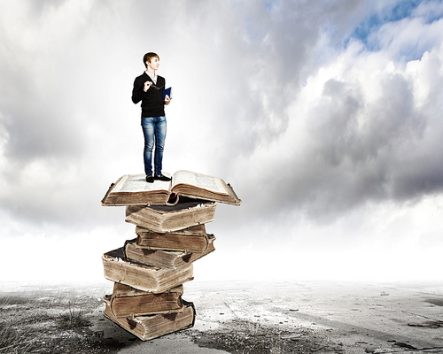 Image of little cute boy standing on pile of books