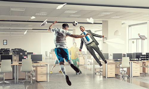 Emotional businessman playing soccer ball in modern office