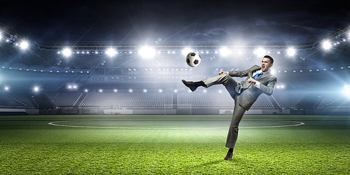 Young businessman in suit playing football at stadium