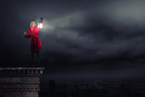 Young blond woman in red cloak with lantern lost in darkness