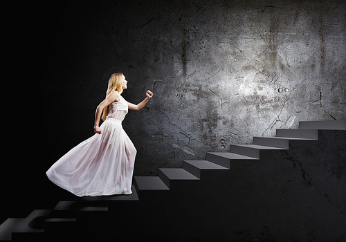 Young woman in white long dress walking up the staircase