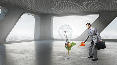 Young cheerful businessman watering green sprout with can