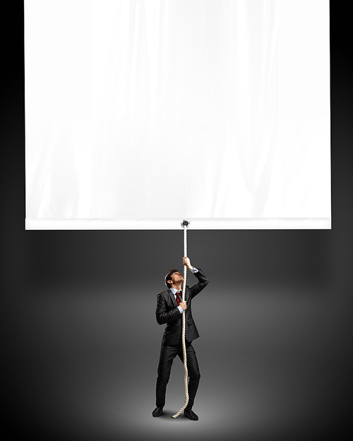 Image of young businessman pulling blank banner. Place for text