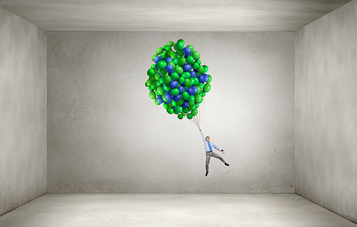 Young successful businessman flying on bunch of colorful balloons