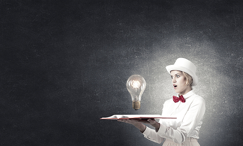 Young woman in white hat with opened book in hands and glass light bulb on pages
