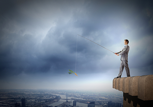 Businessman standing on top of building and fishing with rod