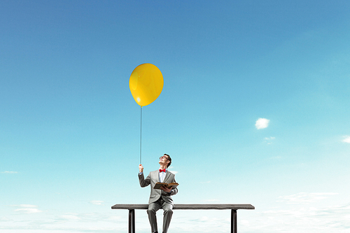 Young businessman sitting on bench with balloon in one hand and book in other
