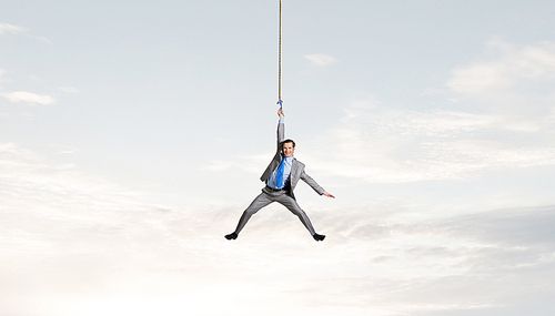 Young businessman hanging on rope high in sky
