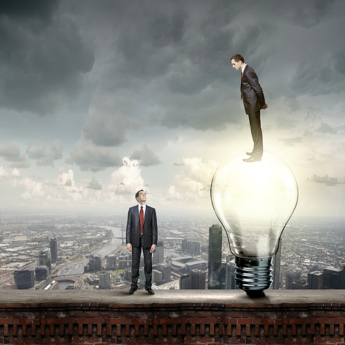 Businessman standing on bulb and looking down at colleague