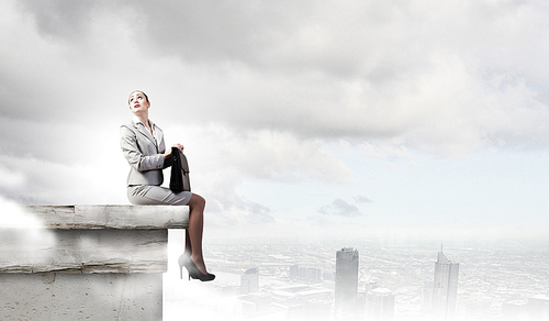 Fearless businesswoman with suitcase sitting on building top