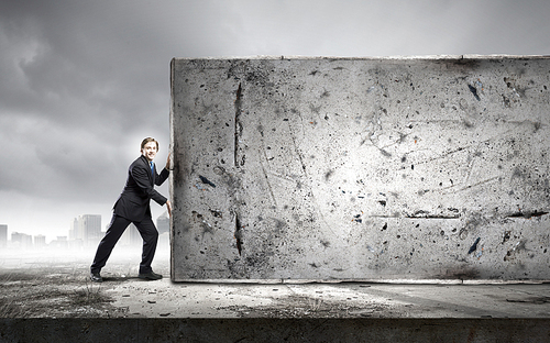 Young businessman making effort to move brick wall