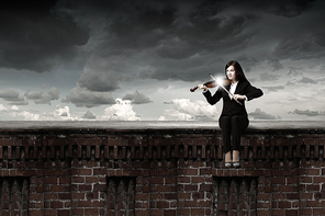 Young woman sitting on building top and playing violin