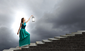 Young woman in green dress with lantern walking in darkness