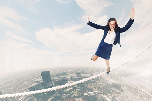 Young attractive businesswoman balancing on rope high in sky