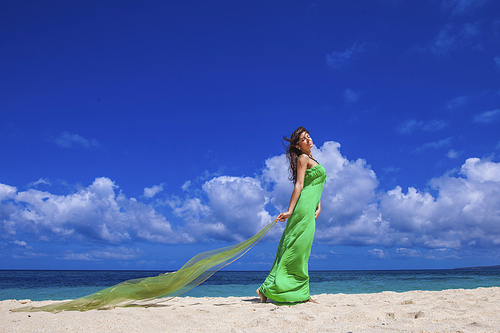Woman in green dress posing with fabric in tropical sea beach