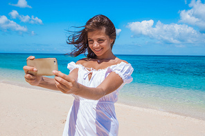 Beautiful happy woman doing selfie with phone on tropical sea beach