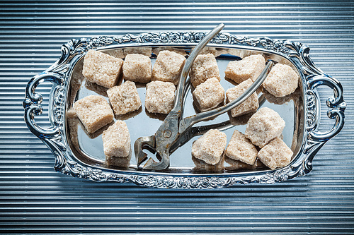 Cane sugar cubes pliers tray on striped background.