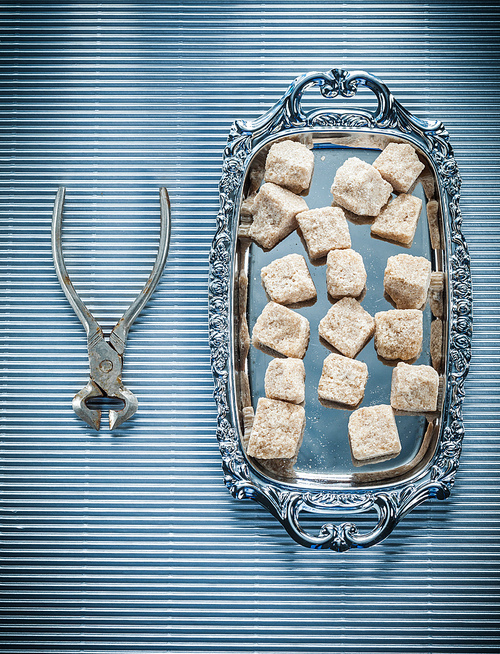 Vintage sugar cubes pliers tray on striped background.