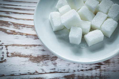 Sugar cubes saucer on vintage wooden board.