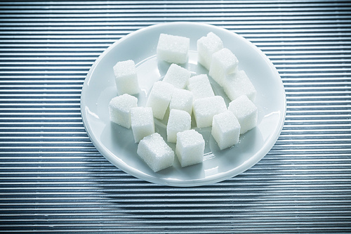 Plate with sugar cubes on striped background.