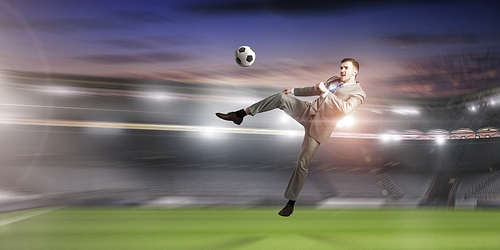 Young businessman in suit playing football at stadium