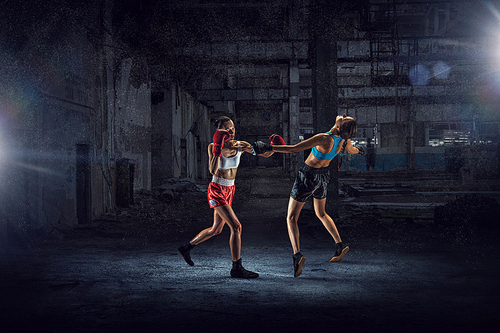 Two young pretty women boxing in desolate building. Mixed media