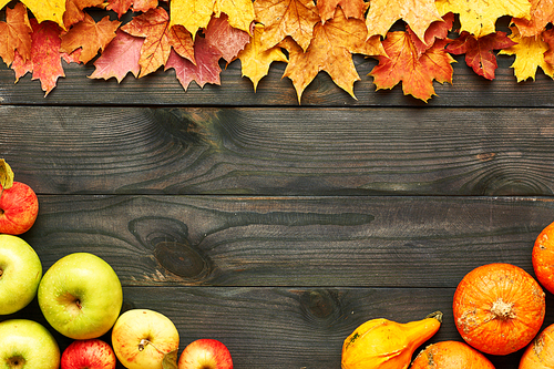 Autumn leaves, apples and pumpkins over old wooden background with copy space