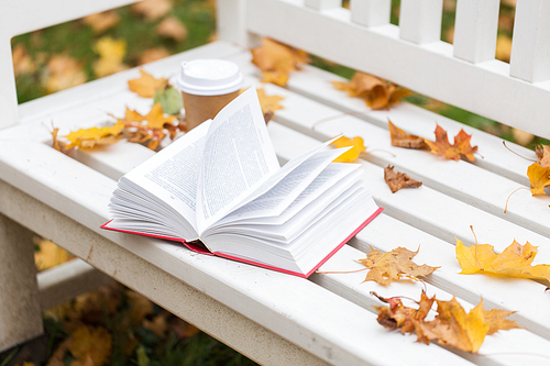 season, education and literature concept - open book and coffee cup on bench in autumn park