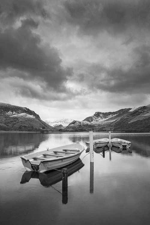 Beautiful  black and white sunrise landscape image in Winter of Llyn Nantlle in Snowdonia National Park with snow capped mountains in background