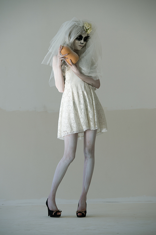 halloween witch. beautiful woman wearing 산타무에르테 mask and wedding dress holding pumpkin posing full length