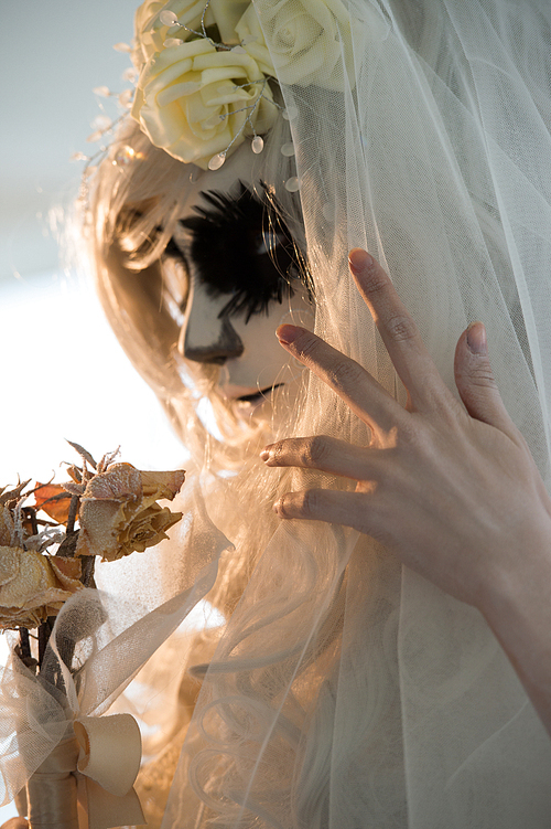 halloween witch. beautiful bride woman wearing 산타무에르테 mask and wedding dress holding dead bouquet of roses