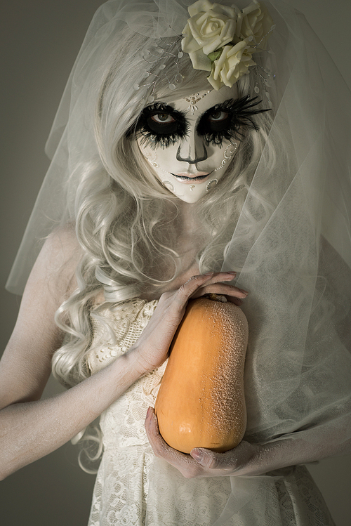 halloween witch. beautiful woman wearing s산타무에르테무에르테 mask holding pumpkin